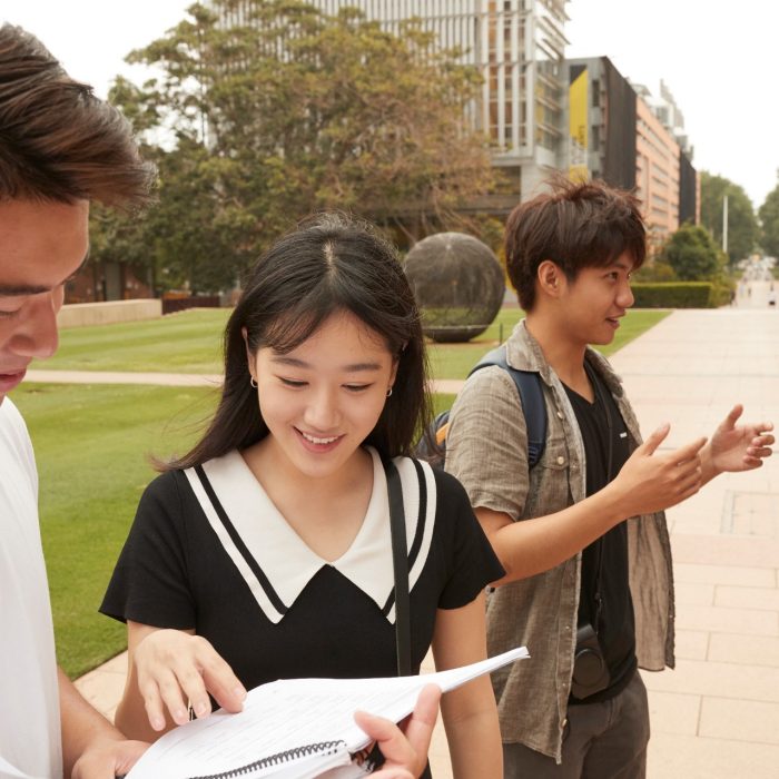 Students with backpacks, headphones, notebooks walking on campus mall