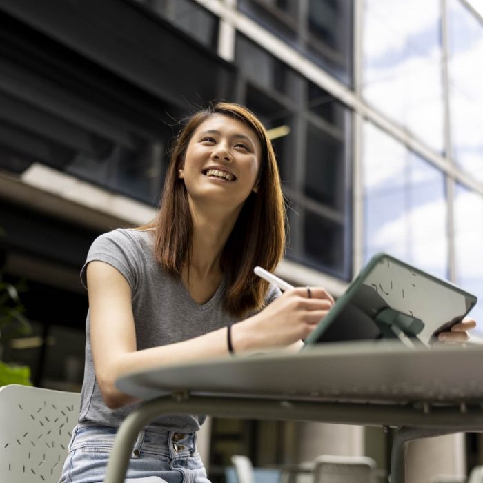 Young female student using iPad and pen in open air courtyard