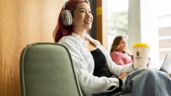 Student with headphones and coffee smiling